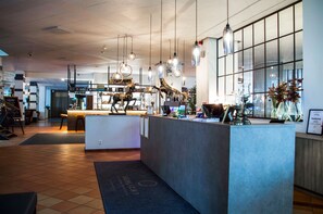 En modern hotellobby med en receptionsdisk, hängande pendellampor och ett stort fönster som ger utsikt över interiören.