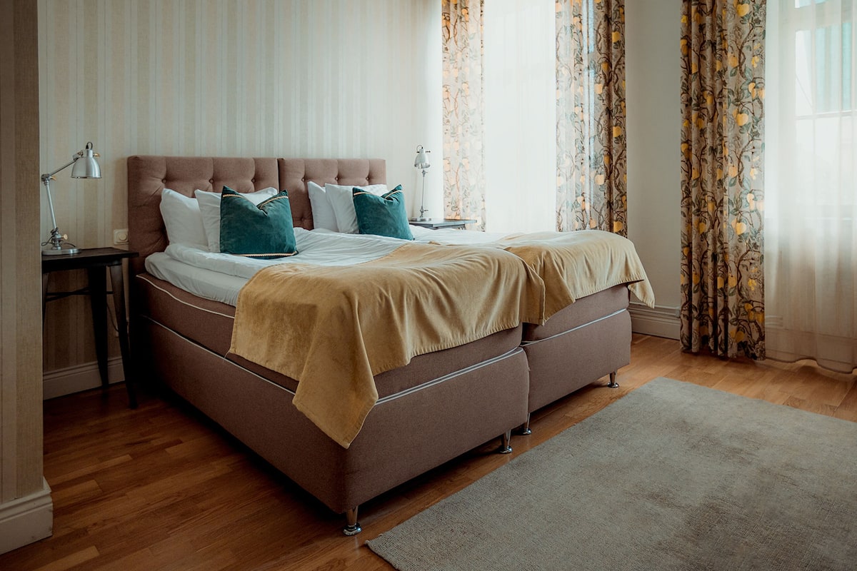 A neatly made bed with a brown headboard, white linens, and teal pillows.