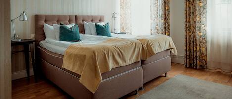A neatly made bed with a brown headboard, white linens, and teal pillows.