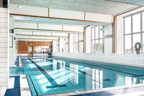 En inomhuspool med kristallklart blått vatten, träbjälkar och stora fönster.