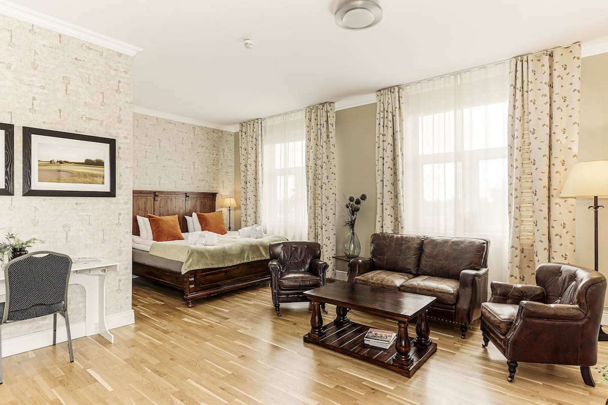 A room with a bed, two leather sofas, a wooden coffee table, and a desk with a chair.