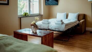 Una habitación de hotel con una cama, una mesa de madera con un jarrón, un radiador, una ventana con vistas y un televisor en la pared.
