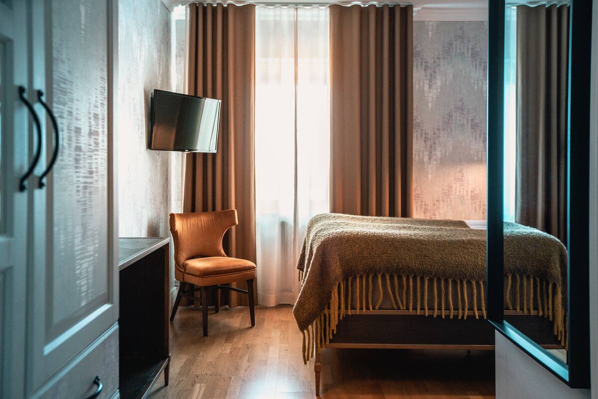 A hotel room with a bed, a chair, a television, and a window with curtains.