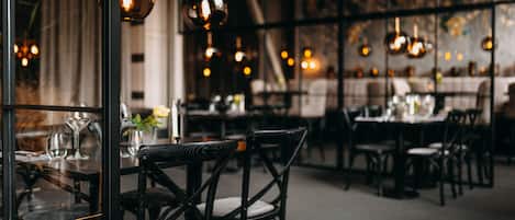 Interior de restaurante con varias mesas y sillas, lámparas colgantes y vistas a través de un separador de vidrio.