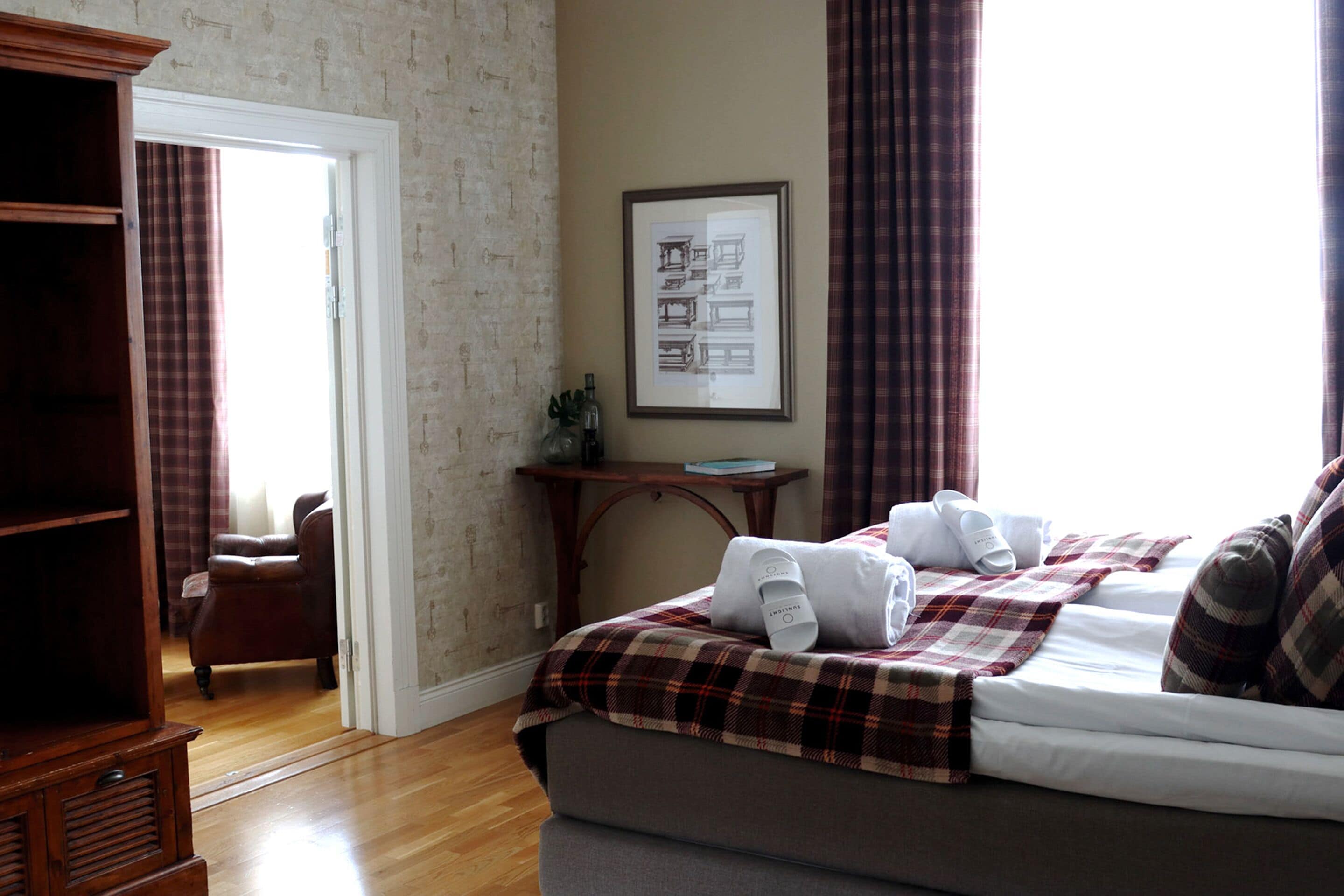 Une chambre d’hôtel avec un lit, une armoire en bois, un bureau avec une lampe et un tableau encadré au mur.