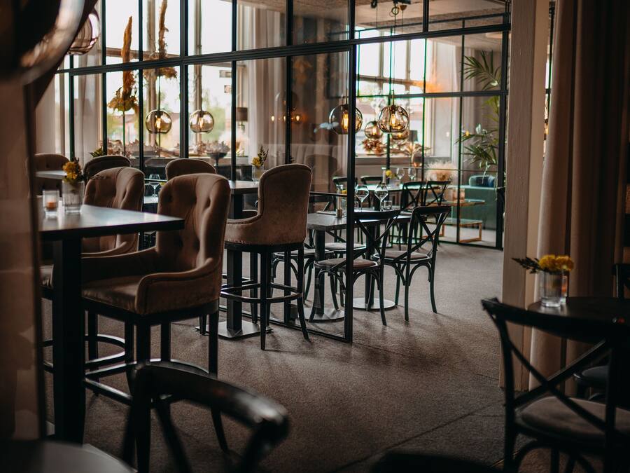 An interior with tables and chairs, large windows, and hanging light fixtures.