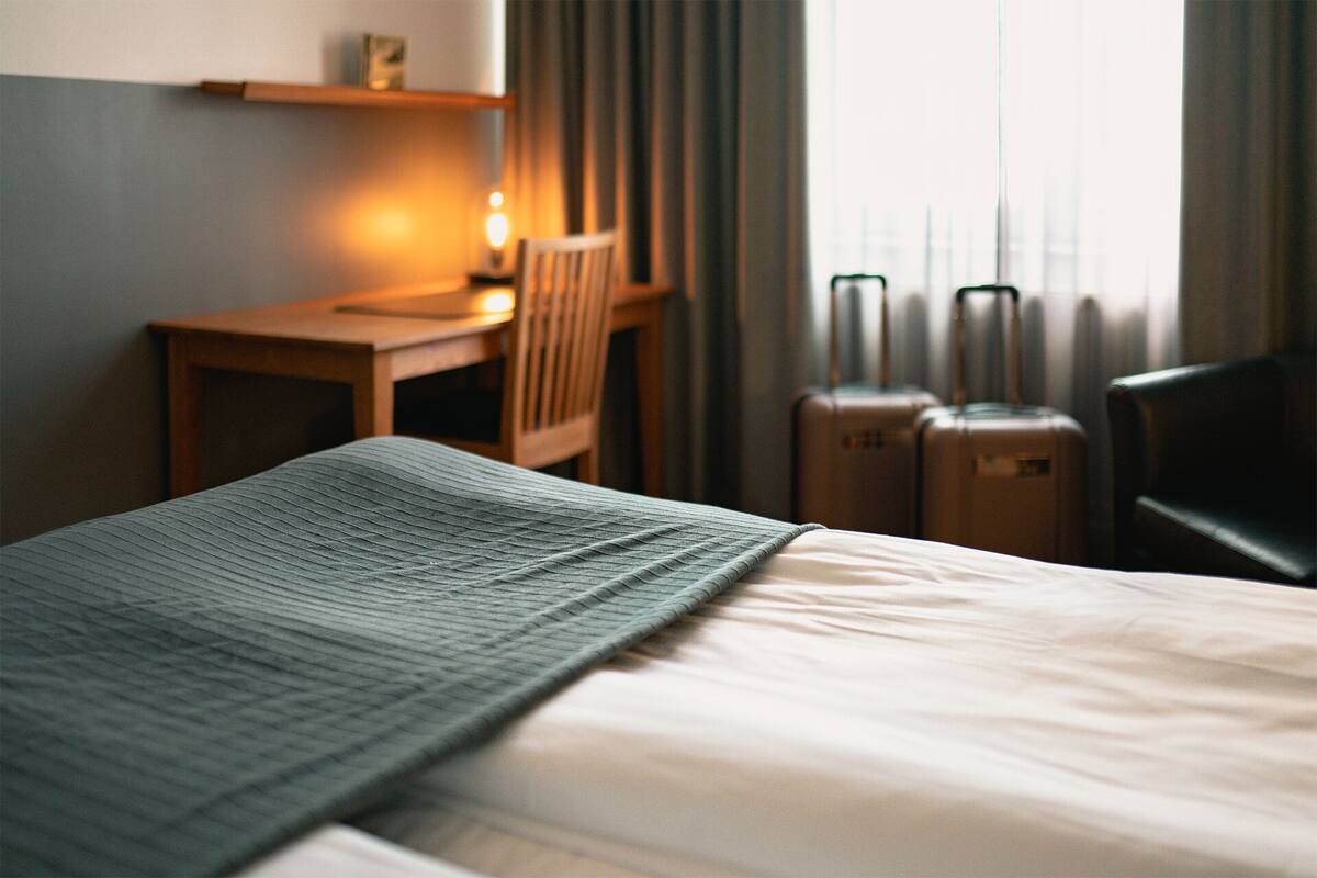 A hotel room with a bed, a desk, a chair, and two suitcases.