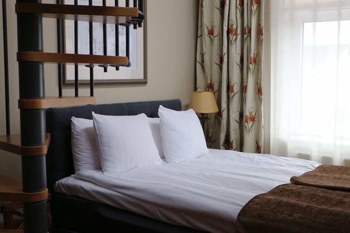 A hotel room with a bed, a wooden headboard, a lamp, and floral curtains.