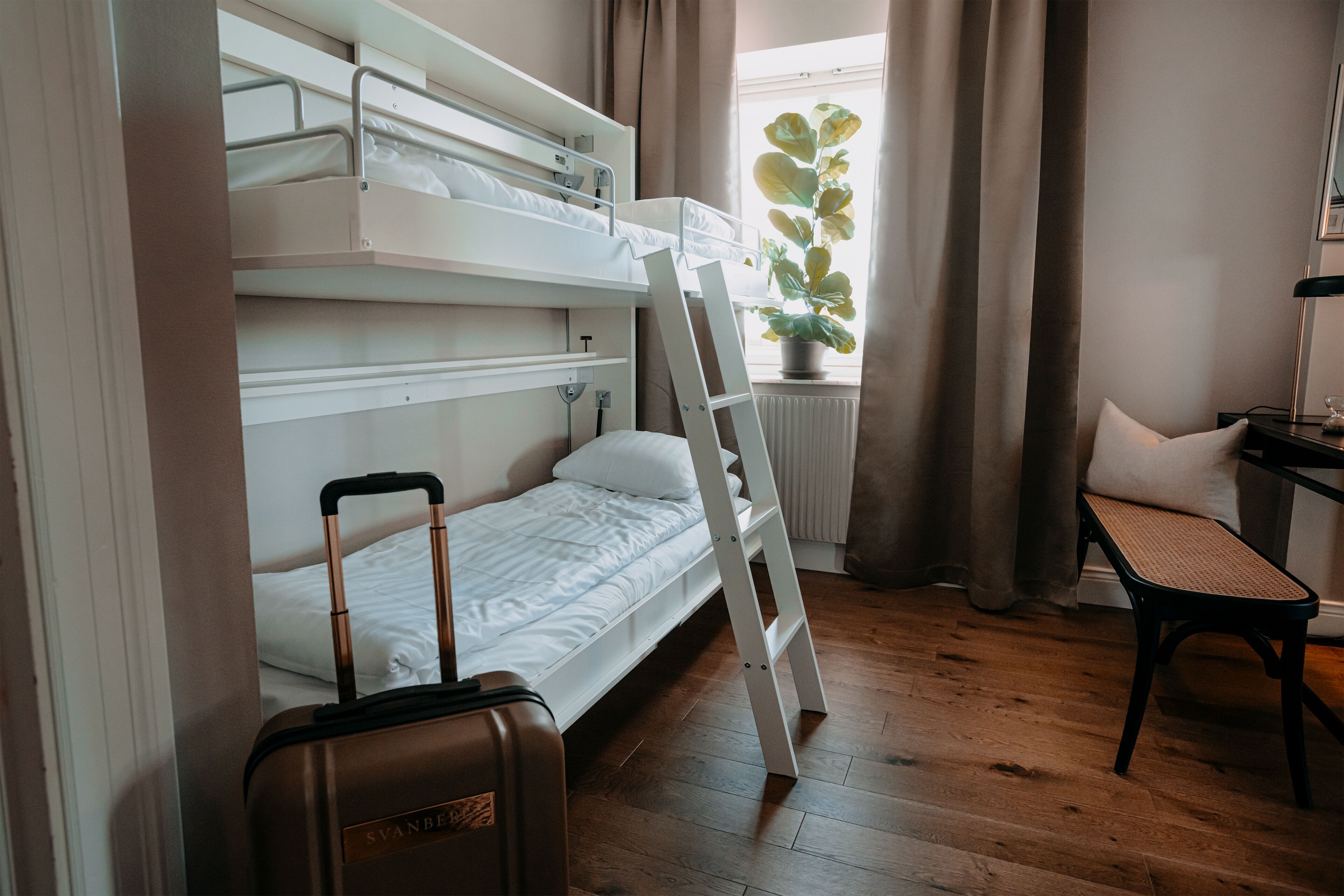 Habitación con literas, una maleta, una escalera, una silla y una ventana con cortinas.