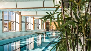 Una piscina con baldosas azul turquesa, rodeada por amplios ventanales y plantas de interior.