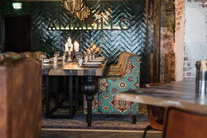 Uma sala de jantar com uma mesa comprida posta para refeição, estofados estampados e design de parede em padrão herringbone.