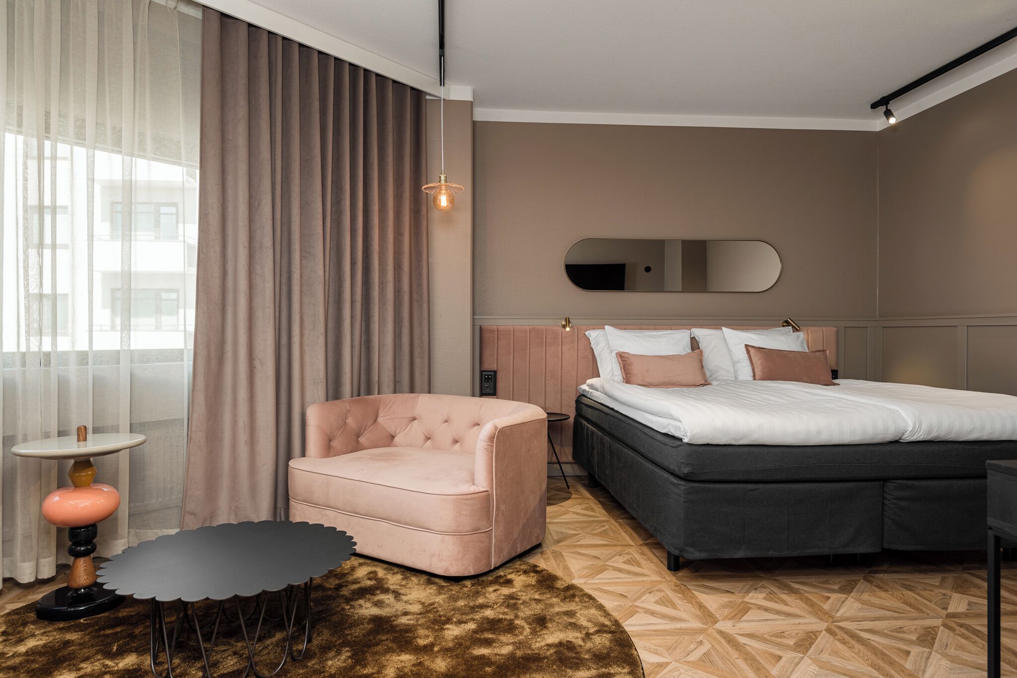 Una camera d'albergo moderna con un letto, una sedia, un tavolino e un'ampia finestra con tende.