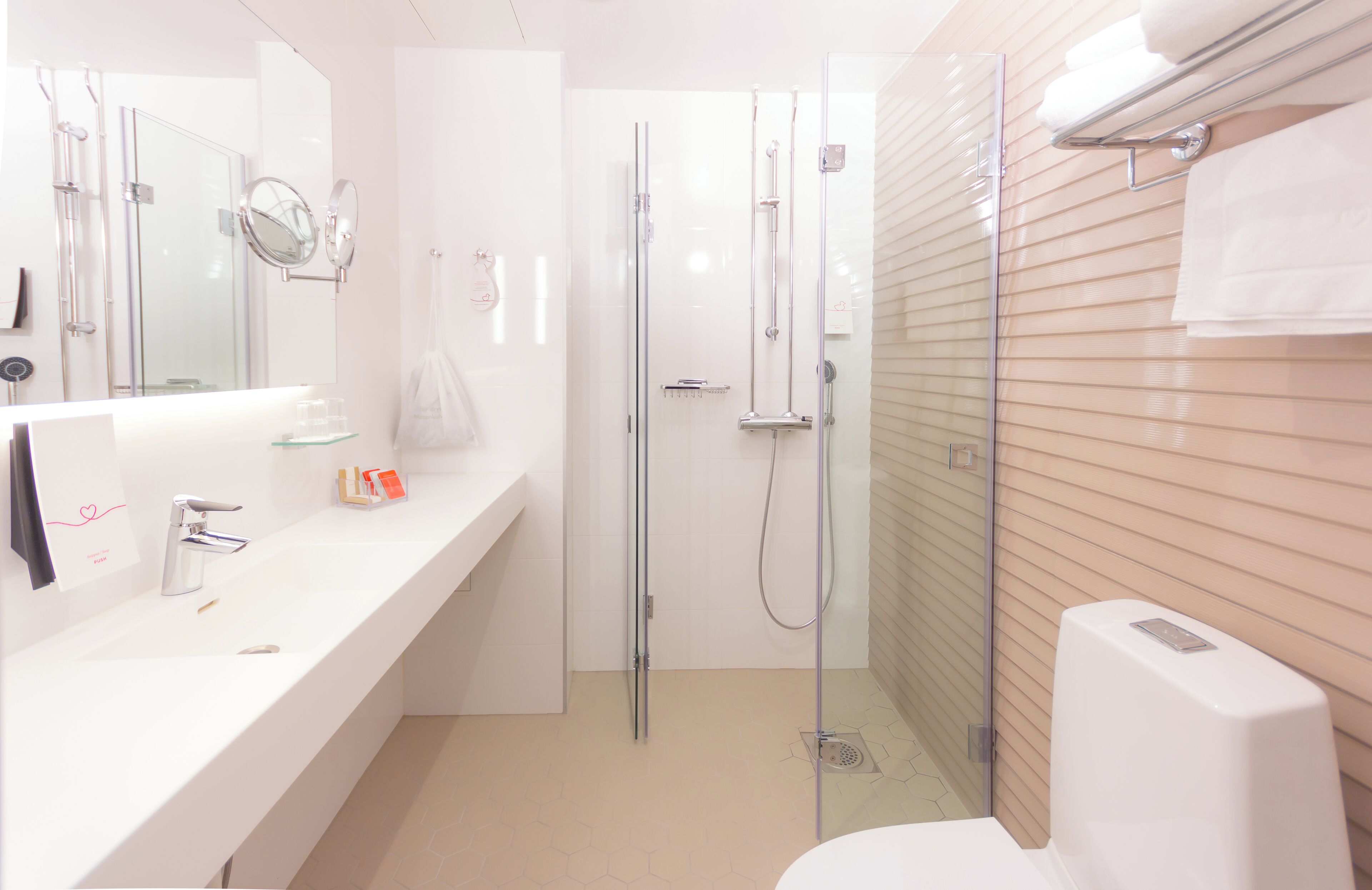 A modern bathroom with a glass-enclosed shower, a white sink with a mirror, and a toilet with a soap dispenser.