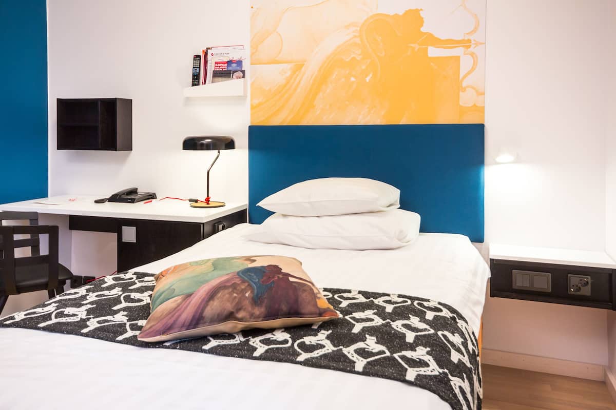 Une chambre d’hôtel avec un lit, un bureau, une chaise et un téléviseur fixé au mur.