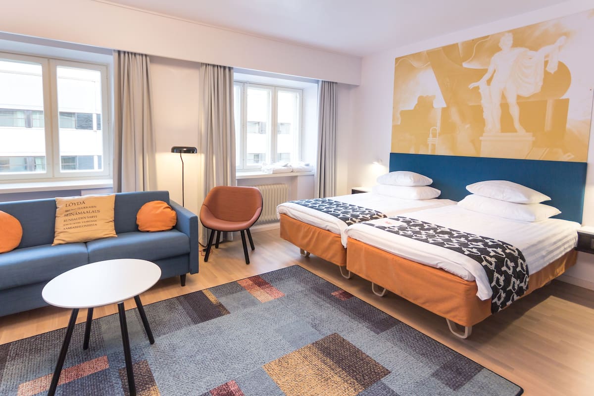 Une chambre d’hôtel avec un lit, un canapé, une chaise, une petite table et une grande fenêtre.