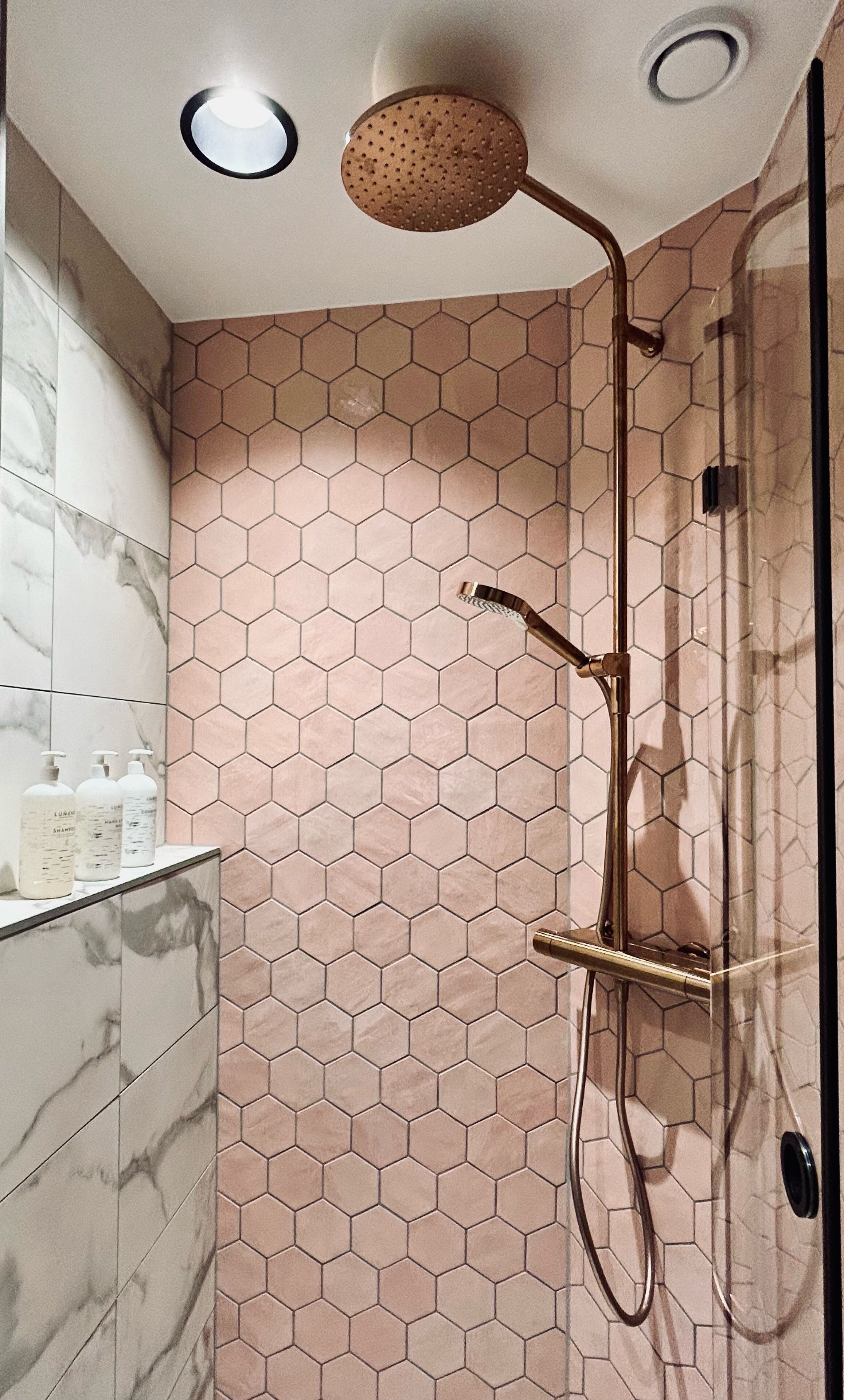 A bathroom with hexagonal patterned tiles, a shower with a gold fixture, and marble tiles on the wall.