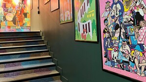 Un escalier recouvert d’une moquette à motifs mène à une pièce ornée d’une fresque murale et de tableaux encadrés.