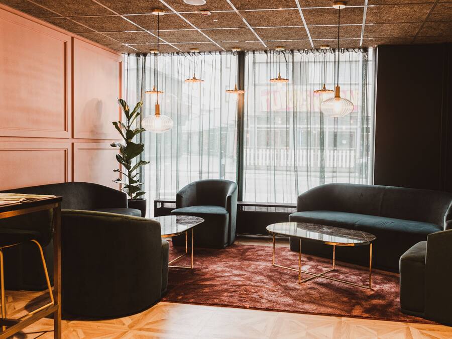 A modern living room with a sofa, two armchairs, a coffee table, and a dining table. There are hanging pendant lights and a large window with sheer curtains.