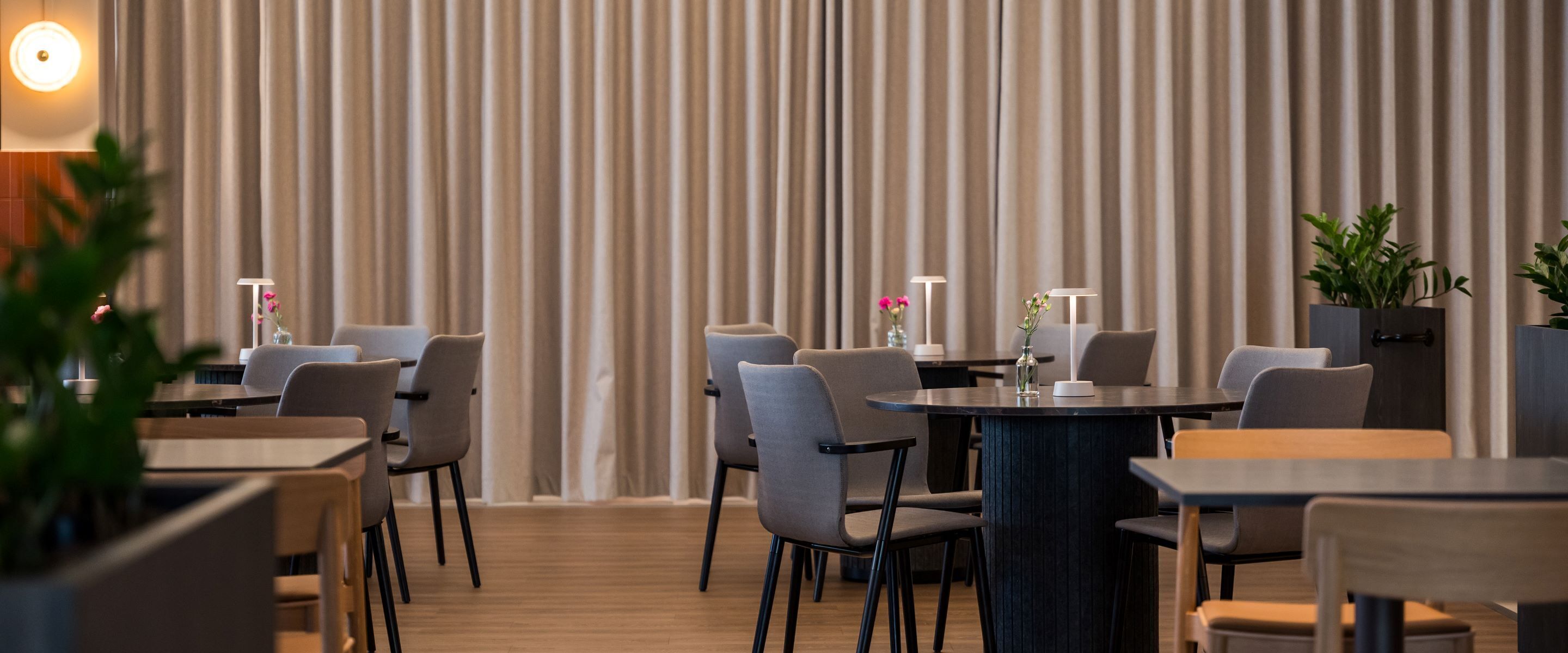 Un comedor moderno con mesas redondas y sillas grises, con un fondo de cortina a rayas y una decoración minimalista.