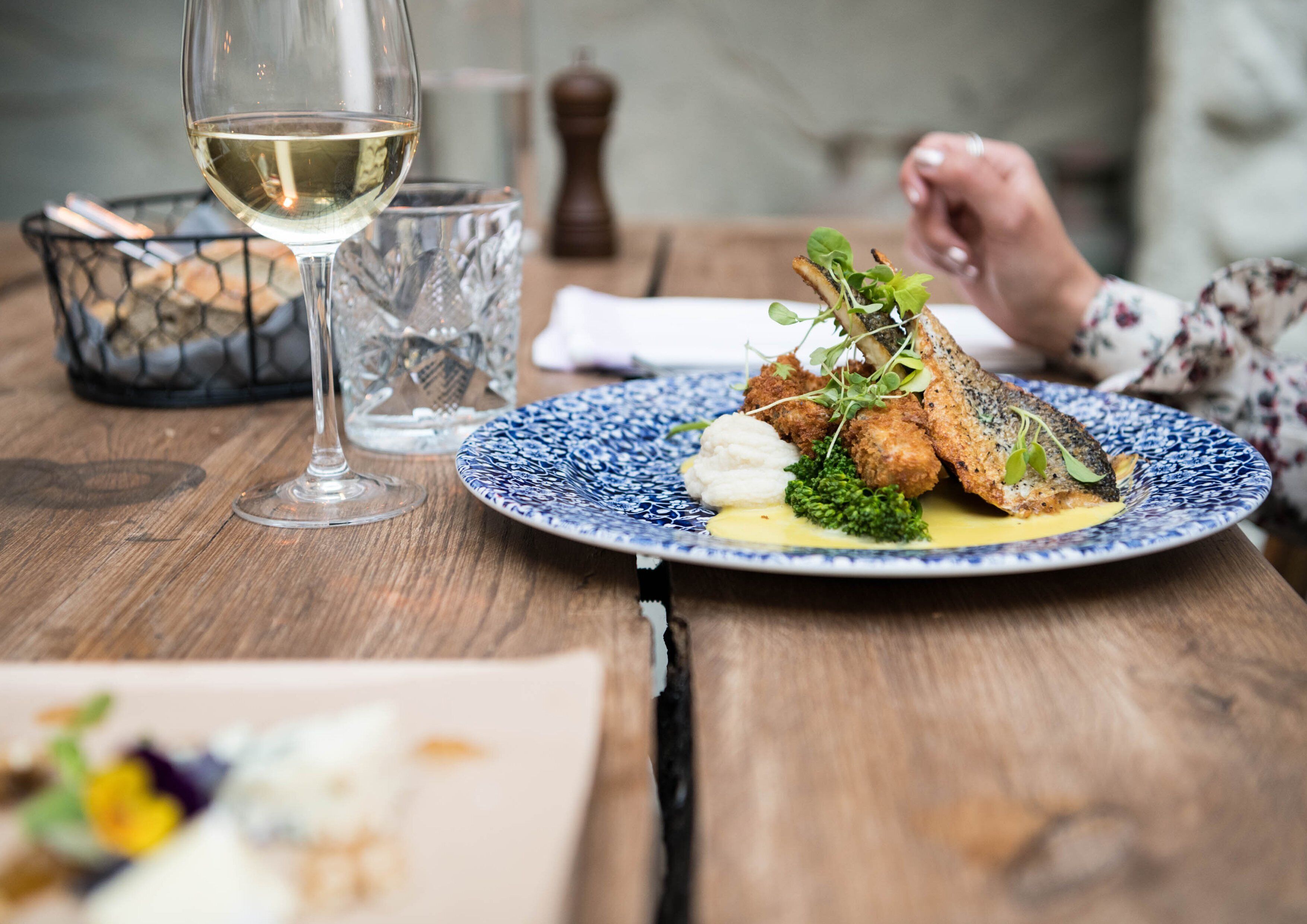 A dining table with a plate of food, a glass of white wine, and a salt shaker.