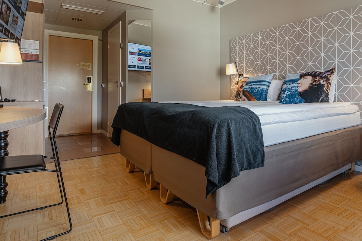 A modern hotel room with a bed, a desk, and a chair.