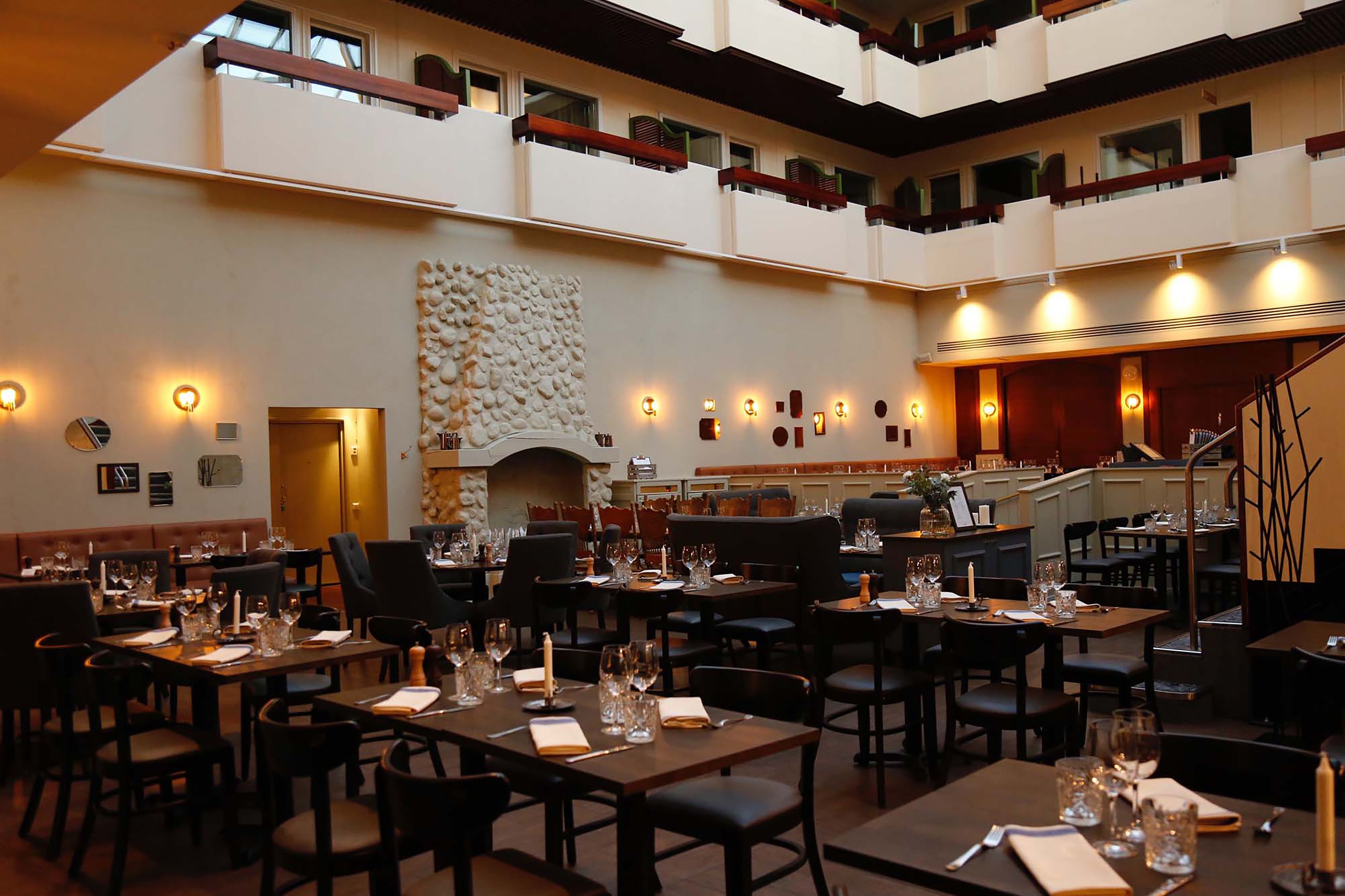 A multi-level dining area with tables set for meals, a fireplace, and a staircase leading to an upper level.