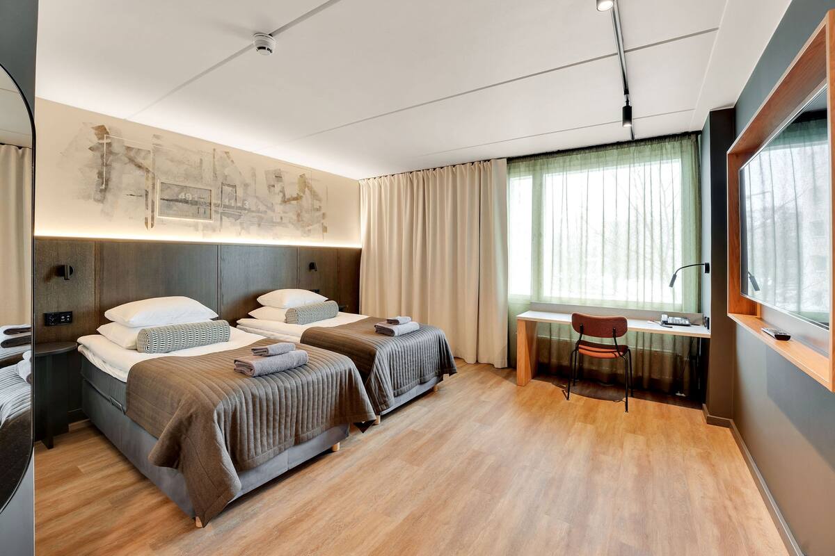 A modern hotel room with two beds, a desk, and a chair.