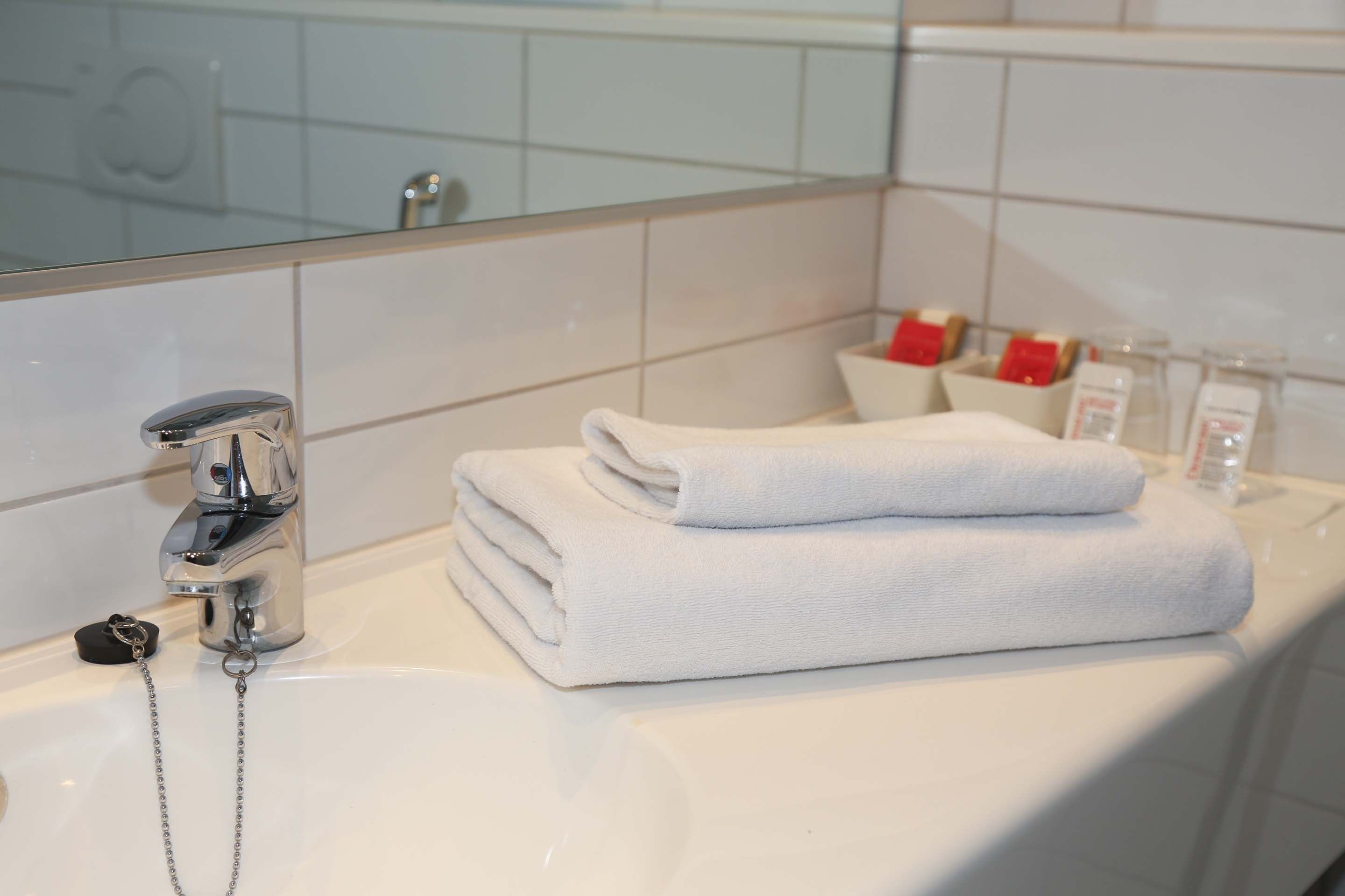 Un baño con lavamanos blanco, un espejo y toallas blancas dobladas con cuidado.