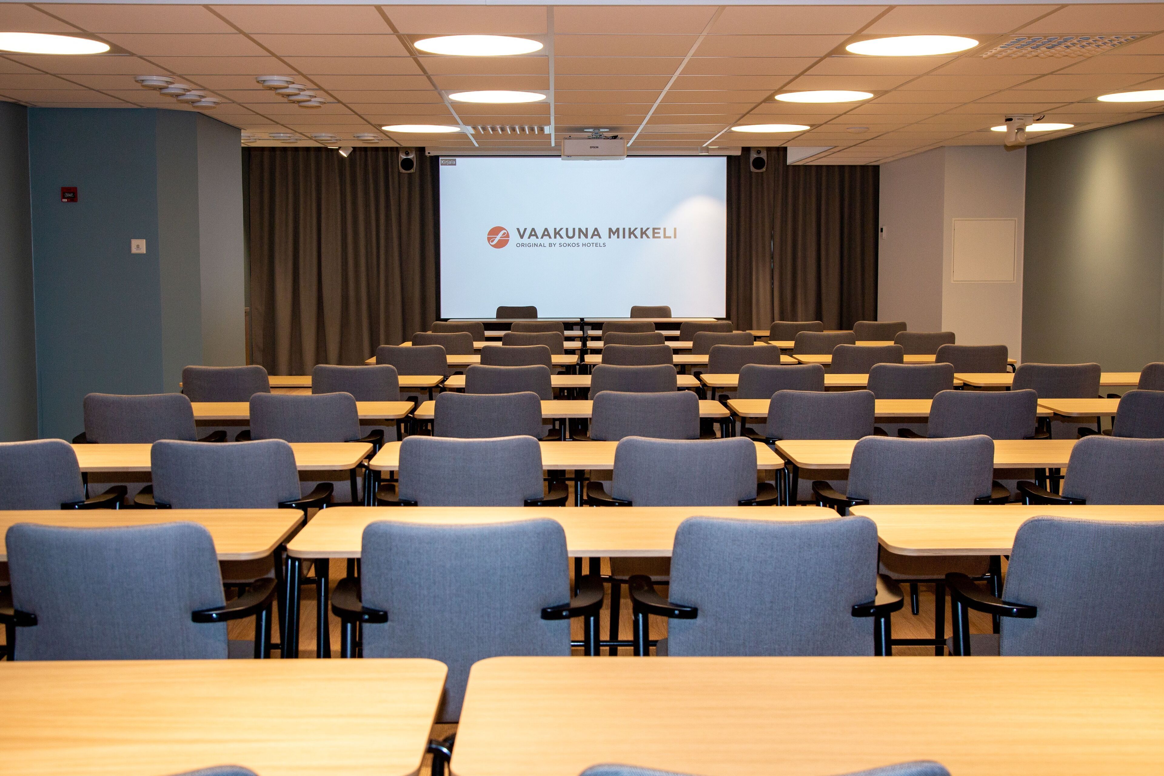 A conference room with rows of tables and chairs, a large screen at the front, and a projector.