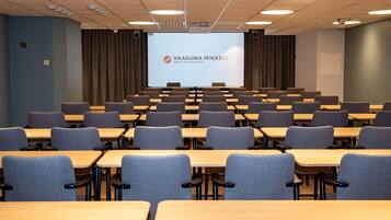 A conference room with rows of tables and chairs, a large screen at the front, and a projector.