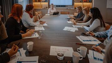 A conference room with a long table, laptops, papers, and a projector screen displaying "VAAKUNA MIKKELI".