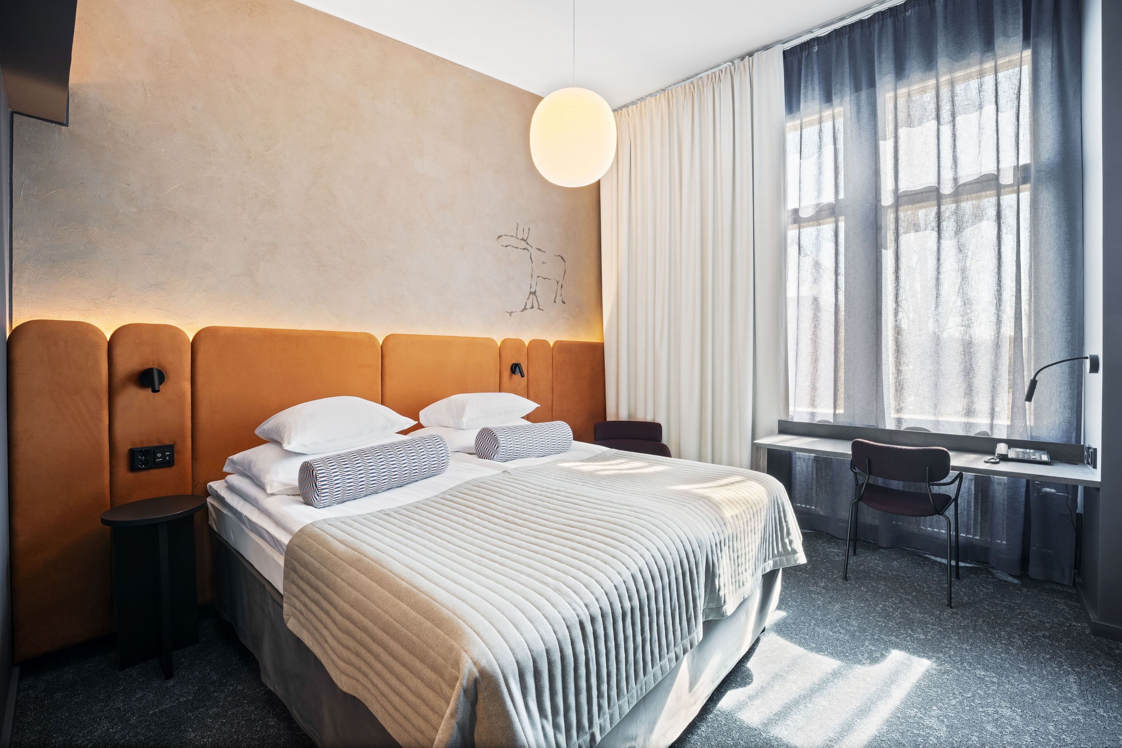 Een moderne hotelkamer met een groot bed, een nachtkastje, een stoel, een raam met gordijnen en een wandlamp.