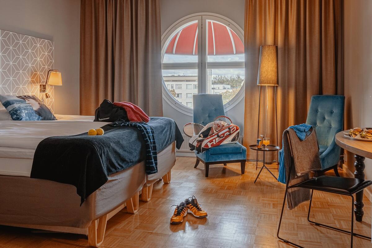 A hotel room with a bed, two chairs, a table with food, and a window with a view.