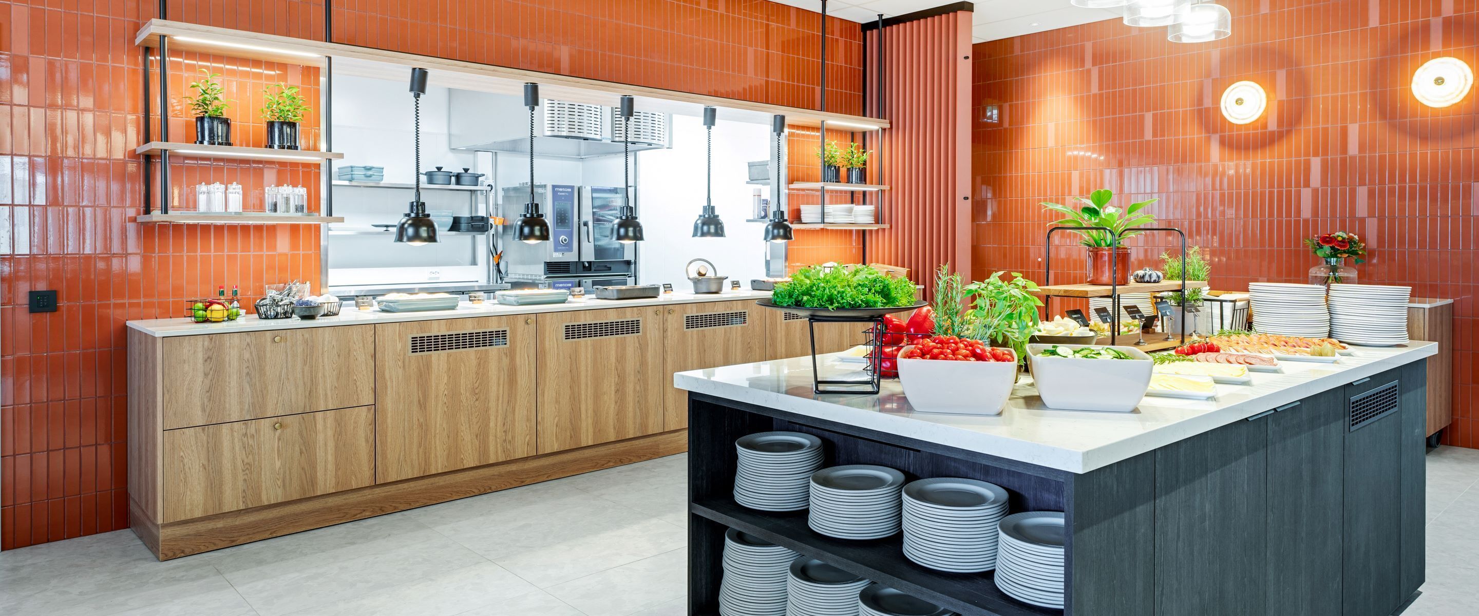 Une cuisine moderne avec des meubles en bois, un îlot central où sont disposés des aliments et un dosseret de carrelage rouge.