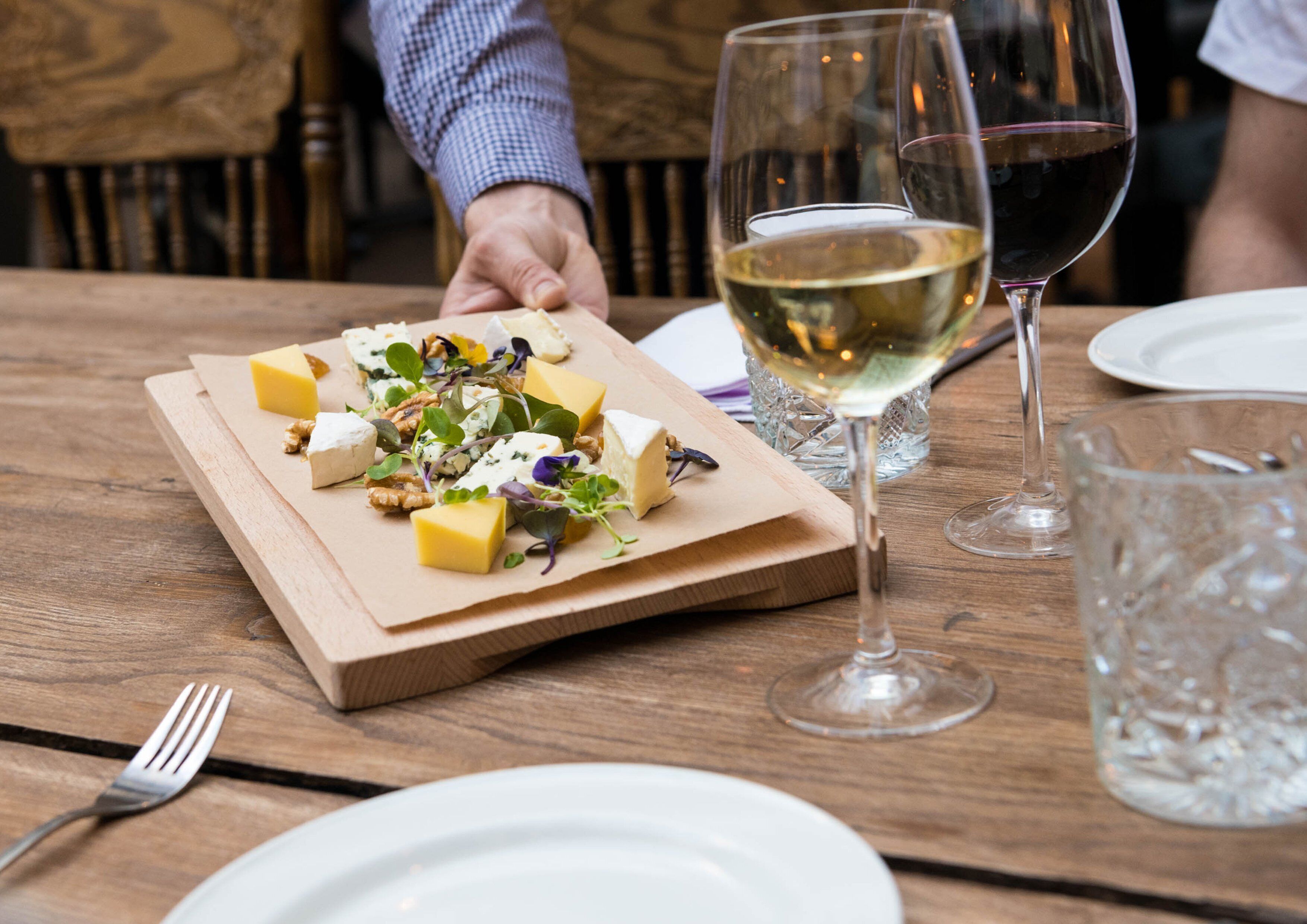 A wooden table with a cheese platter, wine glasses, and a fork.