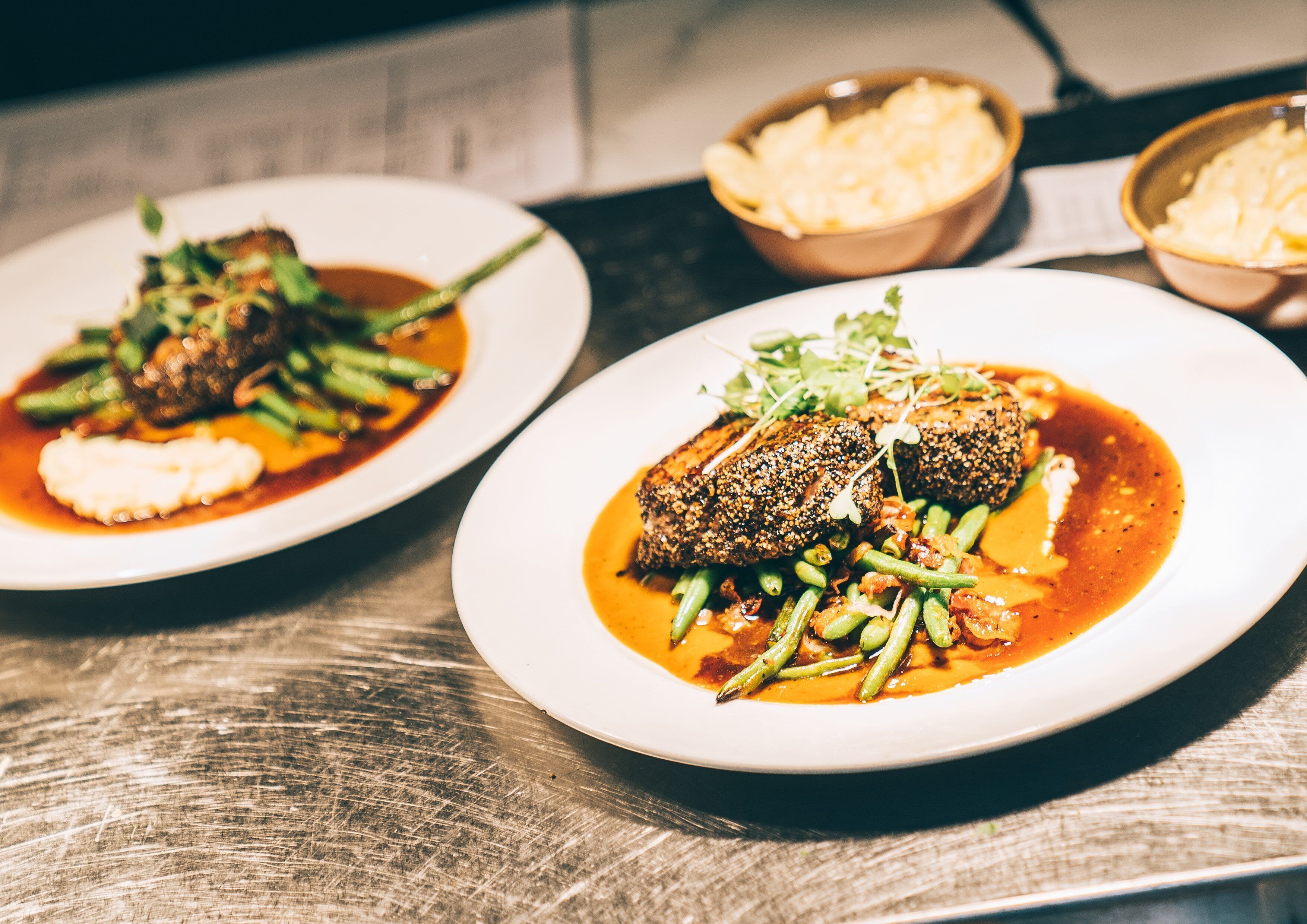 Two plates of food with a variety of vegetables and a sauce, served on a wooden table.