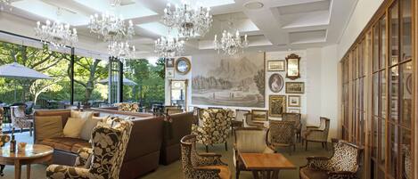A spacious lounge area with multiple seating options, including sofas and patterned chairs, under a high ceiling with chandeliers.