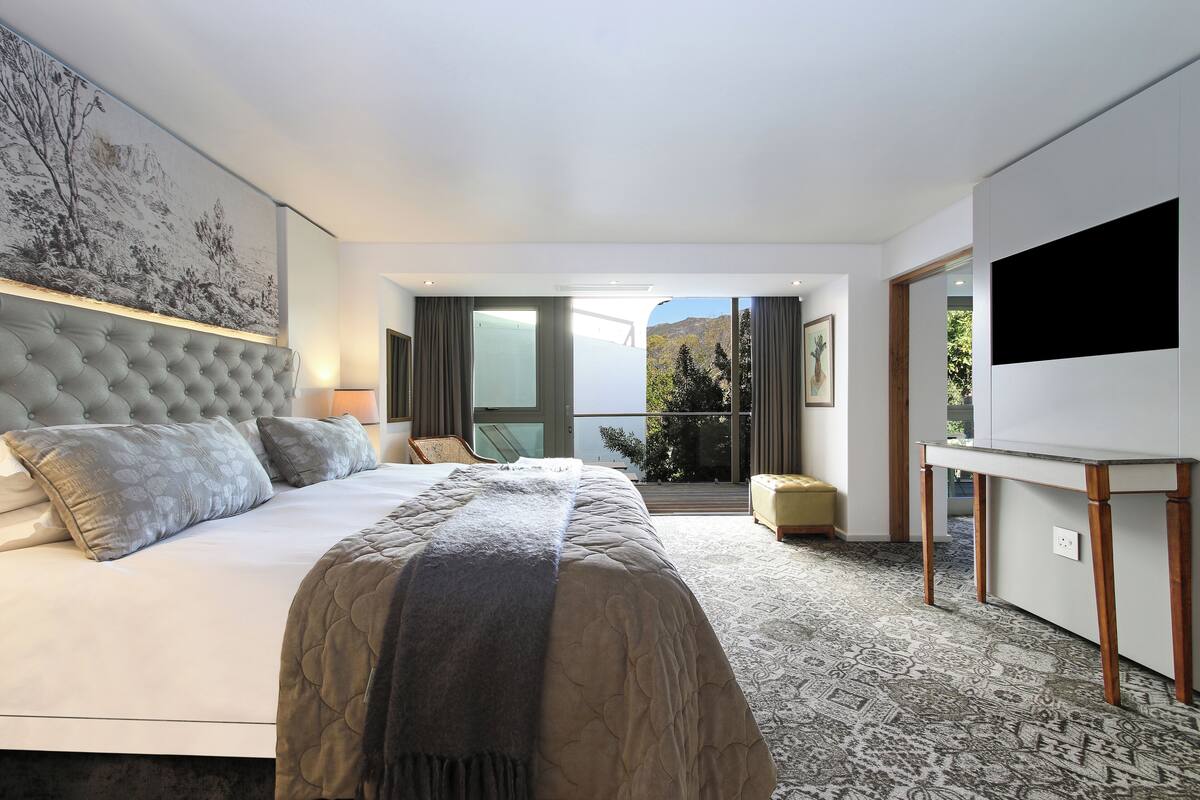A modern hotel room with a large bed, a flat-screen TV, and a balcony with a view of the mountains.