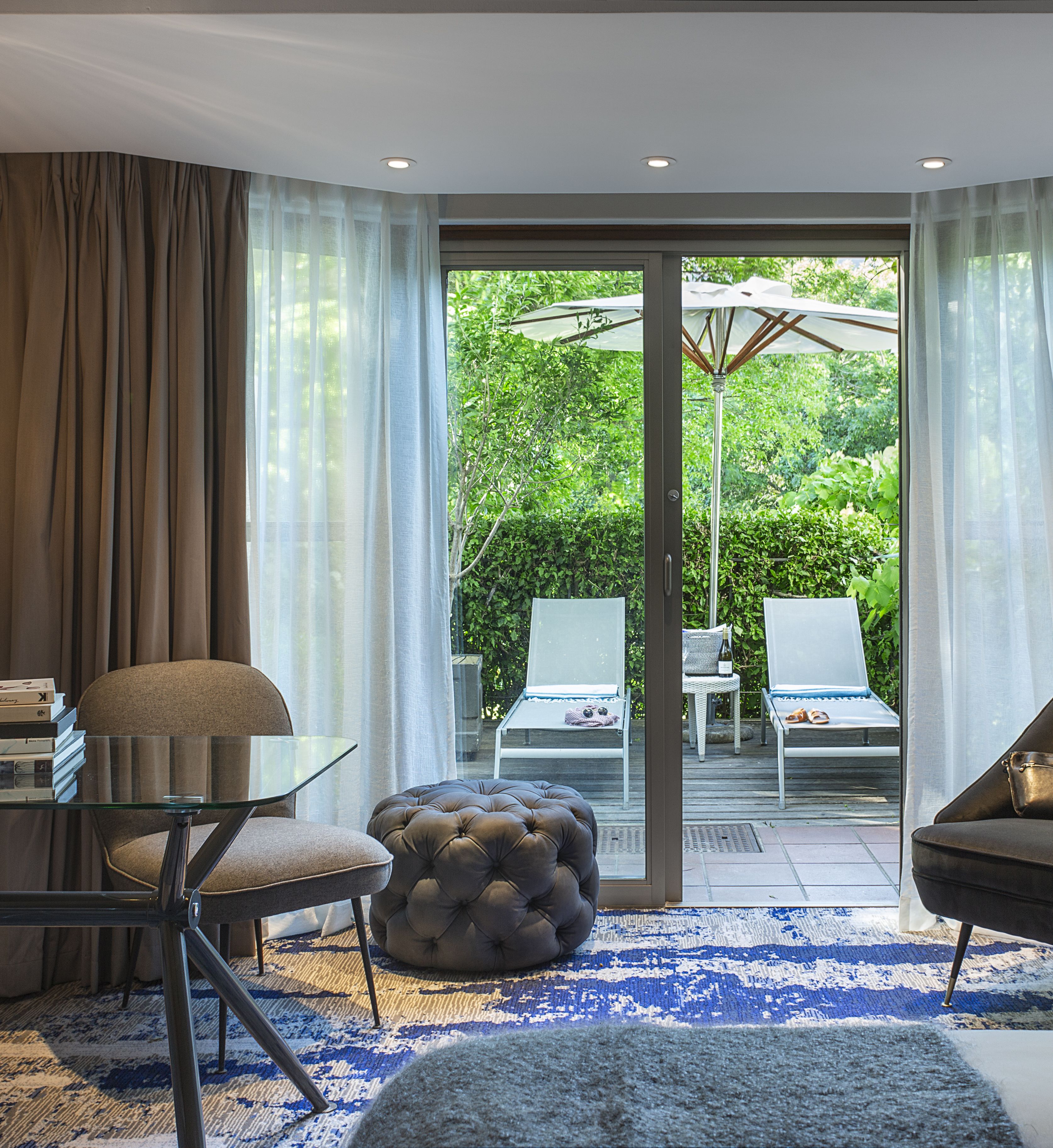 Una sala de estar moderna con una mesa de vidrio, dos sillones, un banquete capitonado y una mesa de centro de vidrio.
