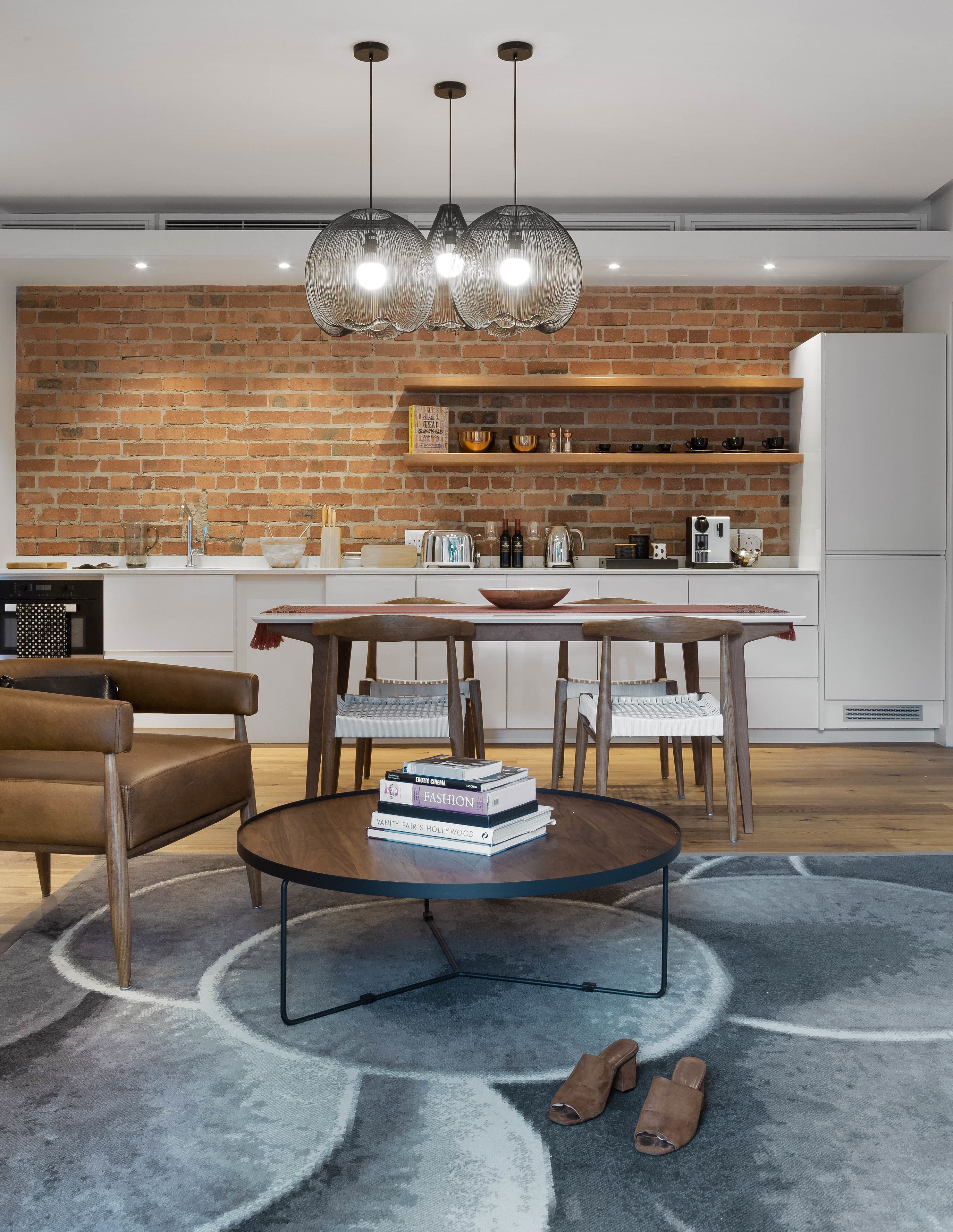 Eine moderne Küche mit Backsteinwand, weißen Schränken und Arbeitsplatte aus Holz. Es gibt einen Essbereich mit rundem Tisch, Stühlen und einem Couchtisch.