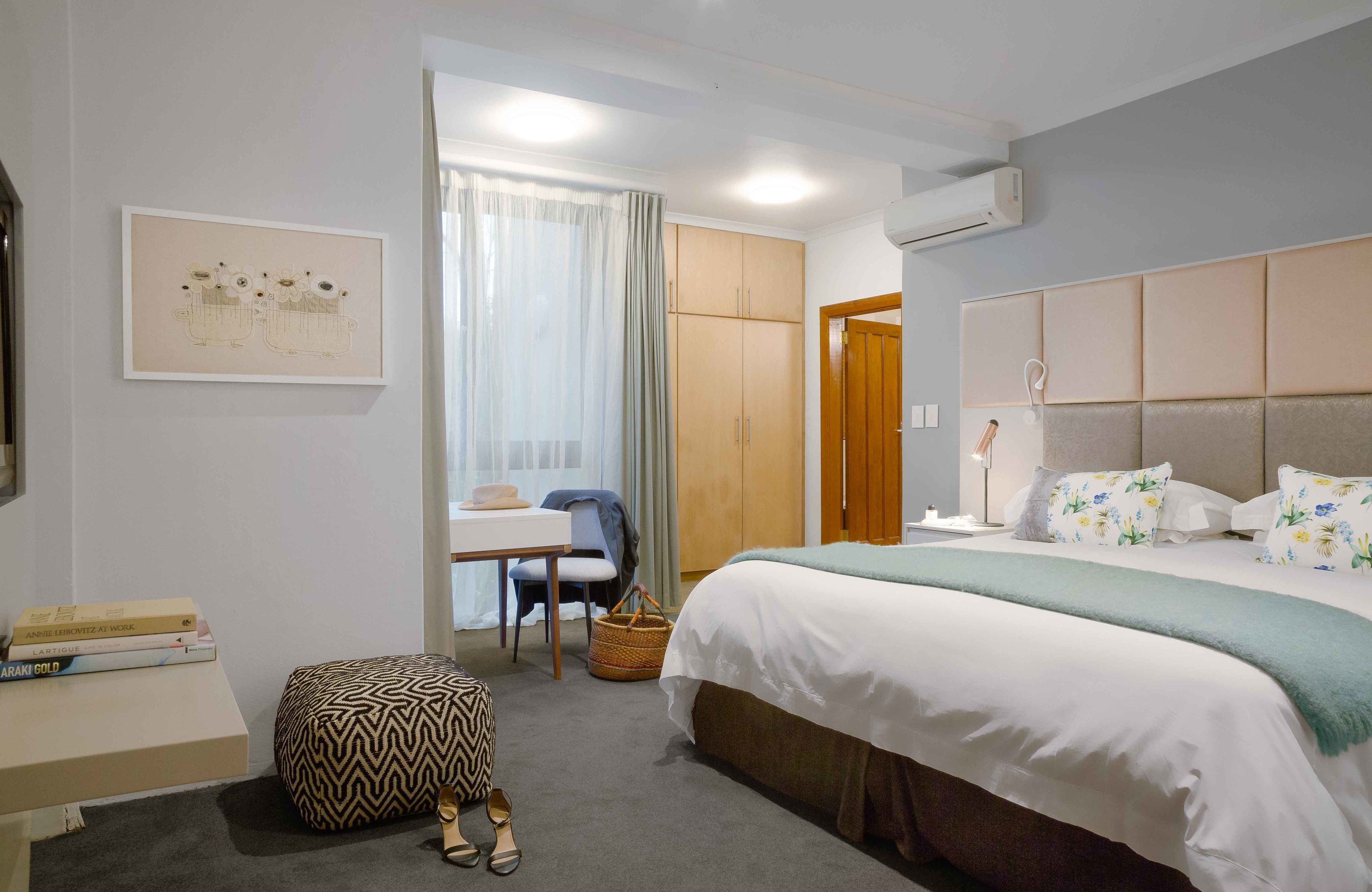 Une chambre d’hôtel équipée d’un lit, d’un bureau, d’une chaise, d’un petit pouf et d’un climatiseur fixé au mur.