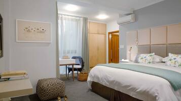 Une chambre d’hôtel équipée d’un lit, d’un bureau, d’une chaise, d’un petit pouf et d’un climatiseur fixé au mur.