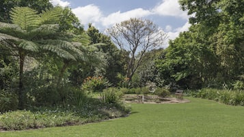 Un jardín bien cuidado con un estanque, bancos y variada vegetación.