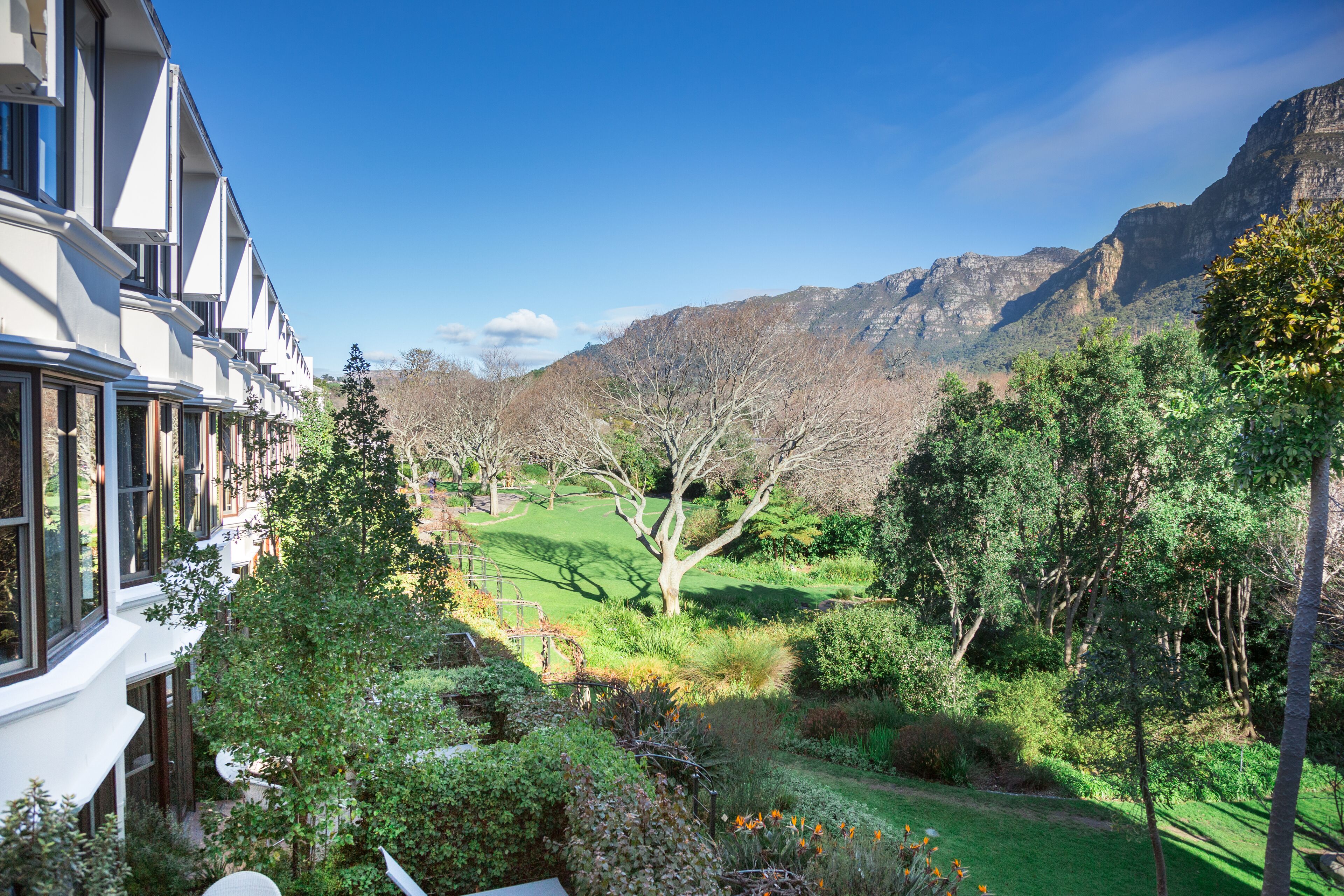 A hotel with a view of a lush garden and mountains.