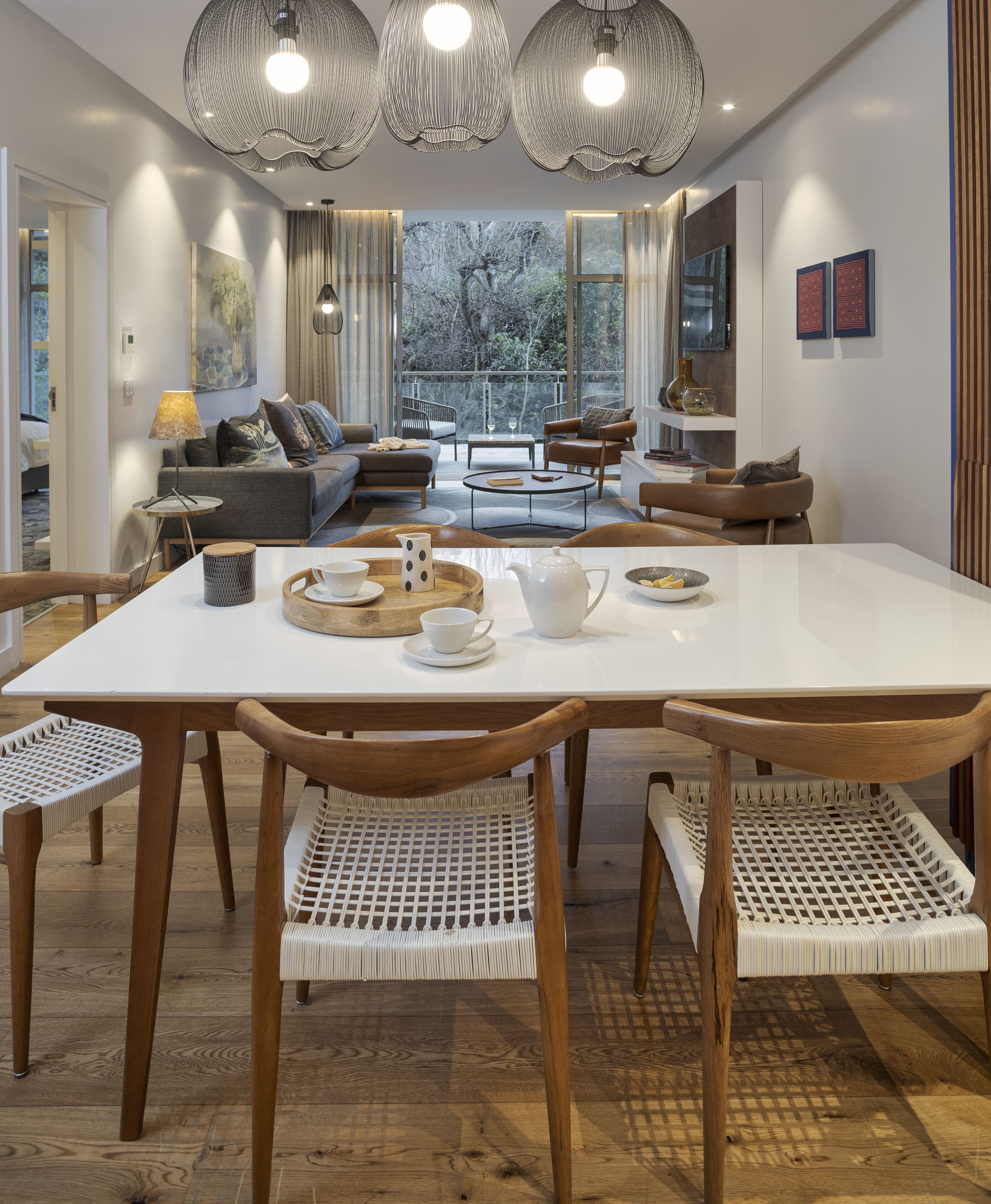 Un comedor moderno con una mesa blanca, sillas de madera y una araña.