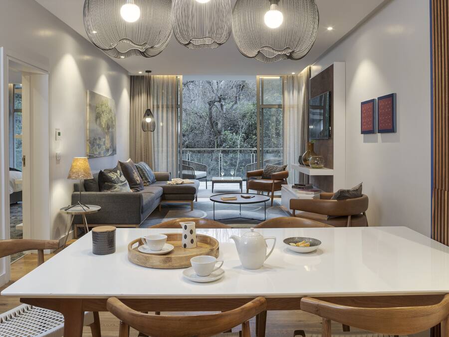 Un comedor moderno con una mesa blanca, sillas de madera y una araña.