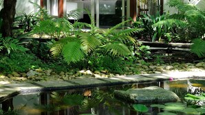 Un jardín interior tranquilo con un estanque, abundante vegetación y una zona de estar con vistas al interior.