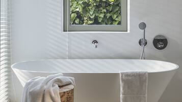 Un baño moderno con una bañera independiente, un taburete de madera y un ventanal con vistas a la vegetación.