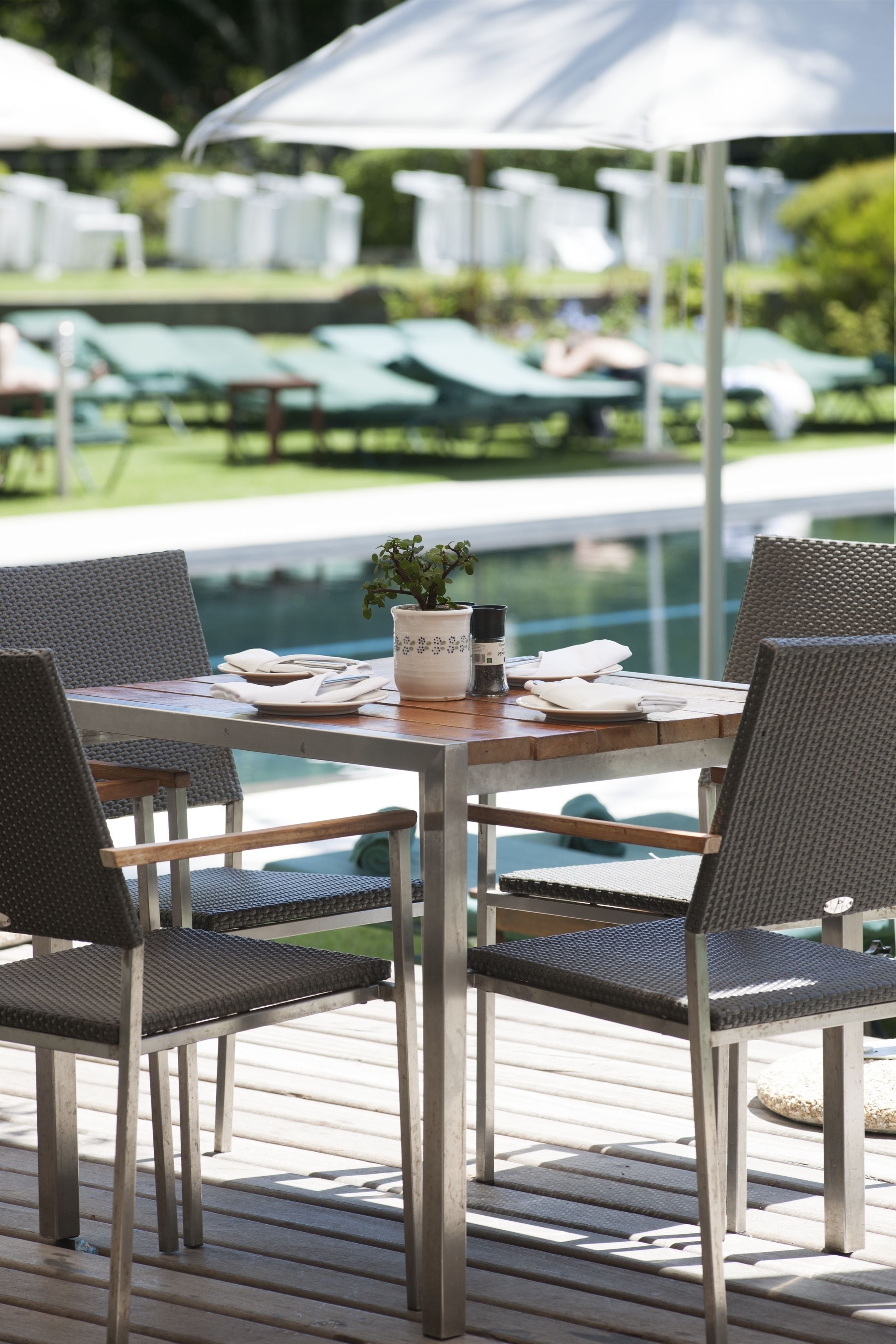 A poolside dining area with a table set for two, surrounded by wicker chairs.