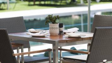 A poolside dining area with a table set for two, surrounded by wicker chairs.
